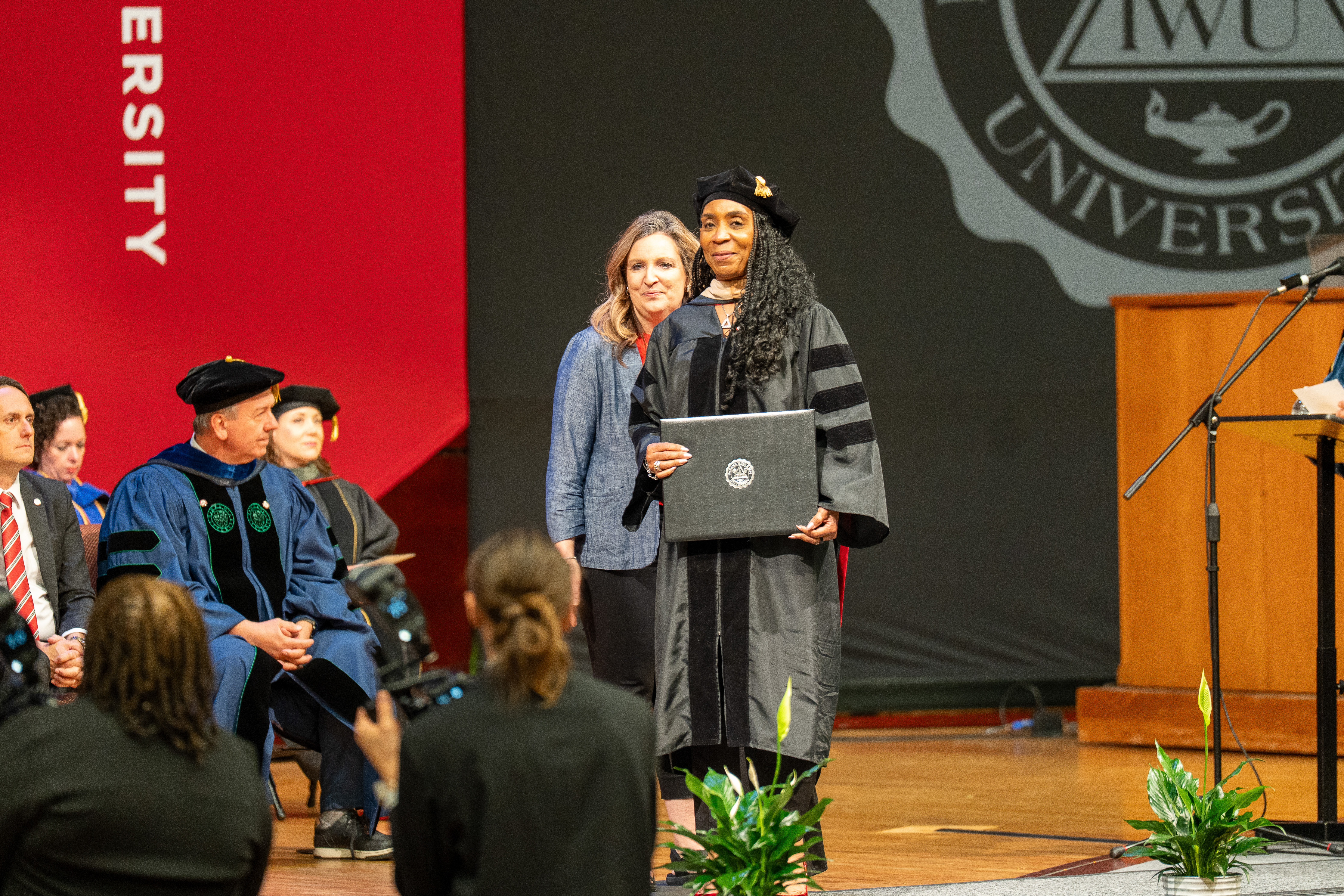 Graduate posing on stage with her diploma at a university commencement