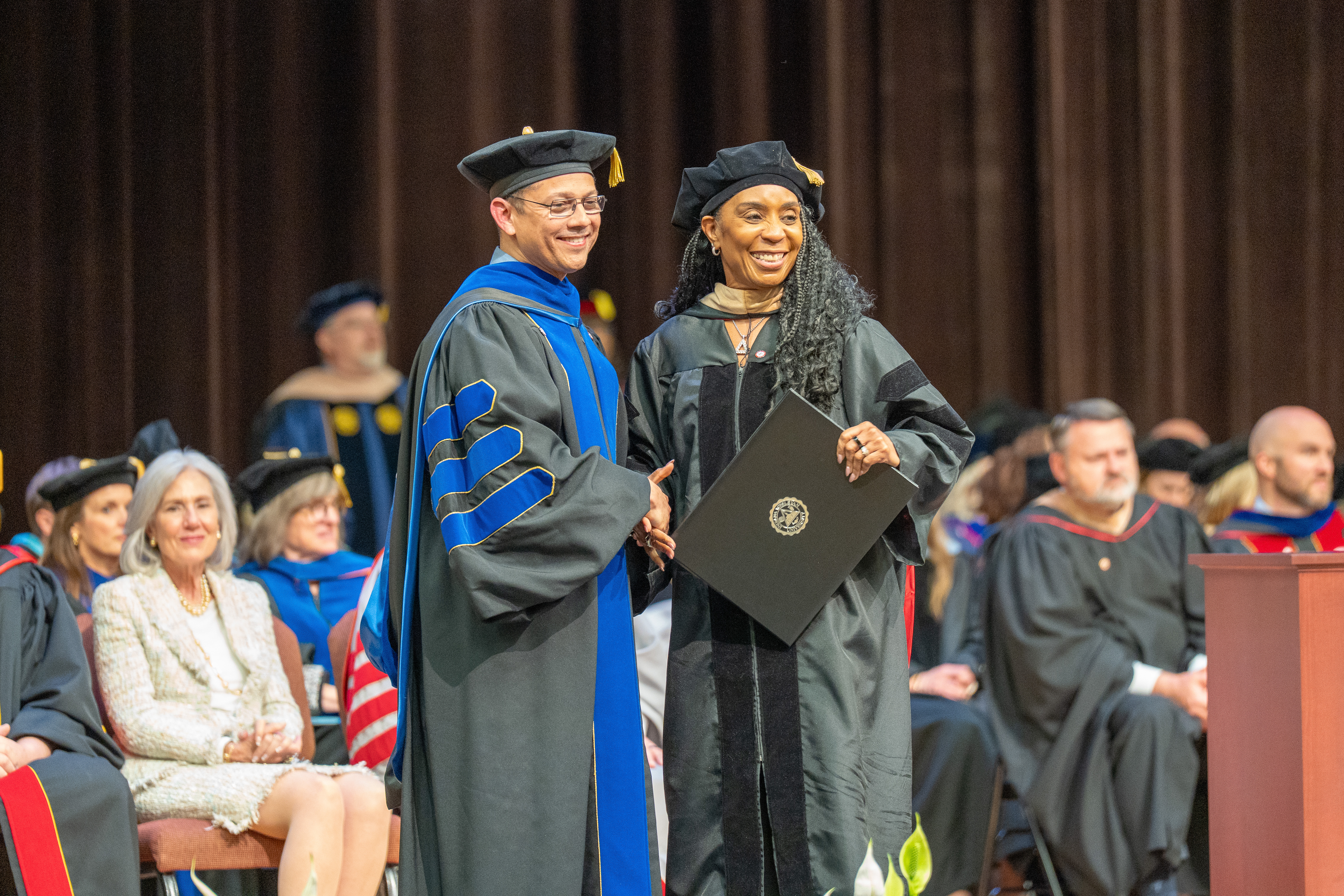Three graduates in academic regalia posing together on stage